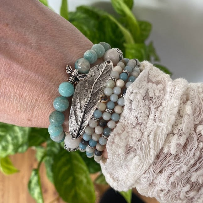 Women's wrist with multiple aqua colored gemstone bracelets including a bee charm and a leaf